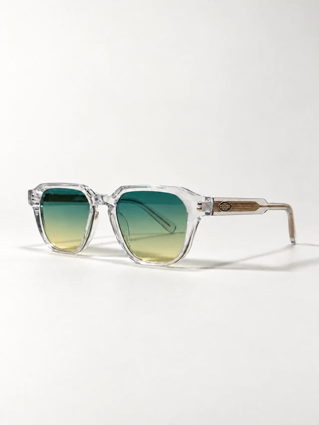 Auracle AUR-001 C5. Low three-quarter view of clear square sunglasses with green gradient lenses and gold-tone textured temples.