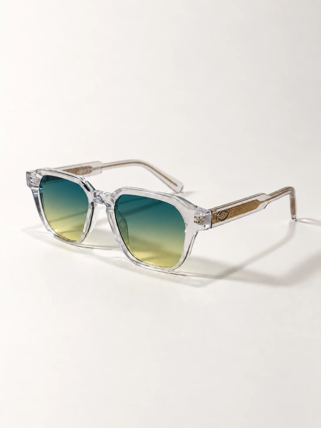 Auracle AUR-001 C5. Three-quarter view of clear square sunglasses with green-to-pale-yellow gradient lenses and gold-tone textured temple inserts.
